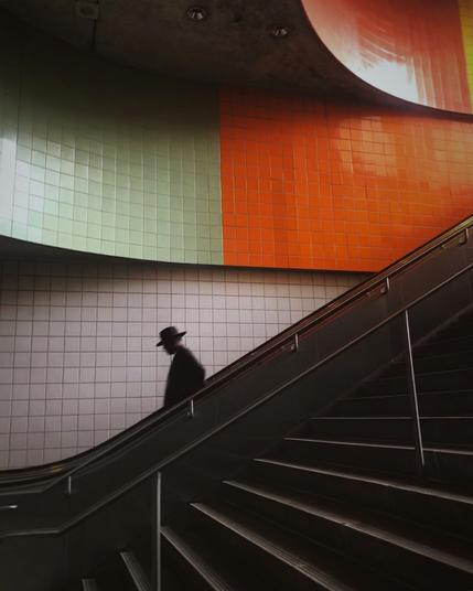 Color photo of man wearing a black hat on metro station escalator.