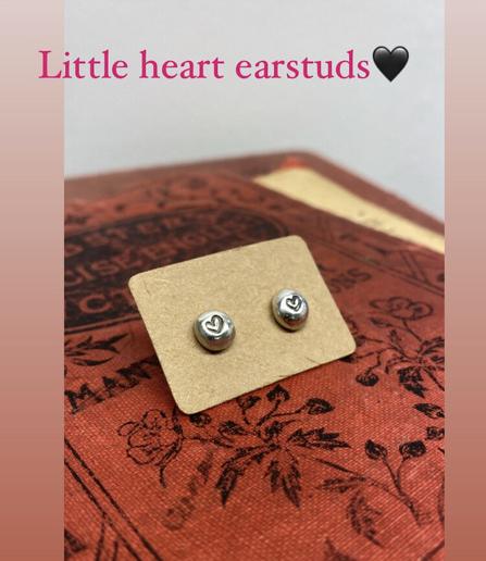Small round silver earstuds with a heart decoration attached onto natural cardboard.