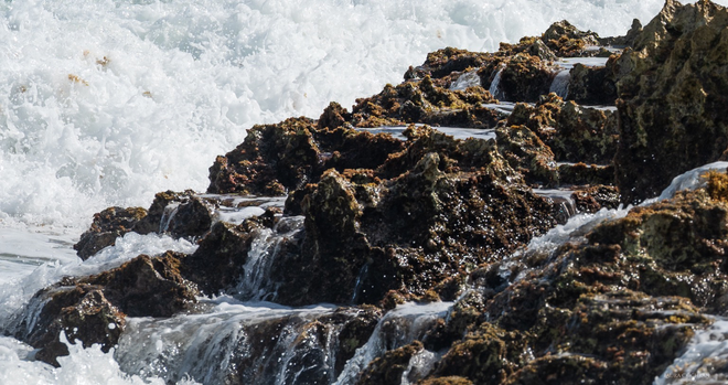 Water cascades done levels of rock while more surf crashes next to it.