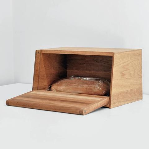 An oak bread box with the door open and a wrapped ciabatta inside.