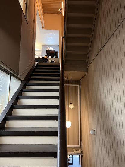 From the landing of a stairwell. Stairs to right go down. Astaire to left go up. An espresso machine is visible at top of the stairs