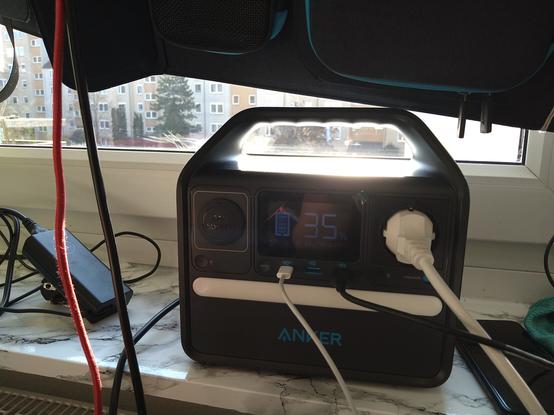 Powerstation of my solar generator charged to 35% with 22 watts input and 7 watts output on a windowsill with lots of cables and the edge of a solar panel visible on top