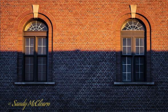 Low morning sun creates a terminator line through the middle of some windows on the side of a brick building.