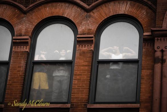 Lads hamming it up in the arched windows of a brick building.