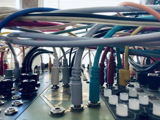 A modular synth covered in multi colored cables viewed from the side. Some modules plugs and buttons are visible