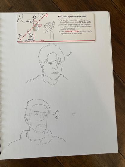 Realistic pencil line sketches of two different people’s heads on a white sketchbook. At the top of the page is a cardboard set of directions for using a camera lucida.