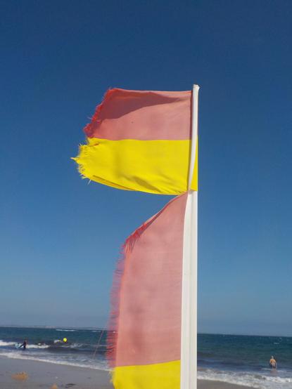 Flag with a red stripe on top and a yellow stripe on the bottom, flying against a bright blue sky