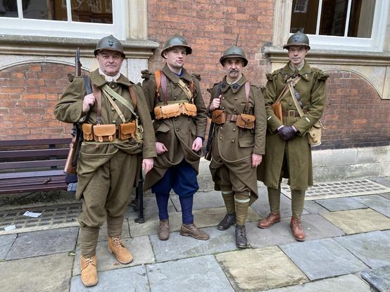 Quatre reconstituers en tenue de soldat français de 1940, devant un bâtiment des briques rouges.