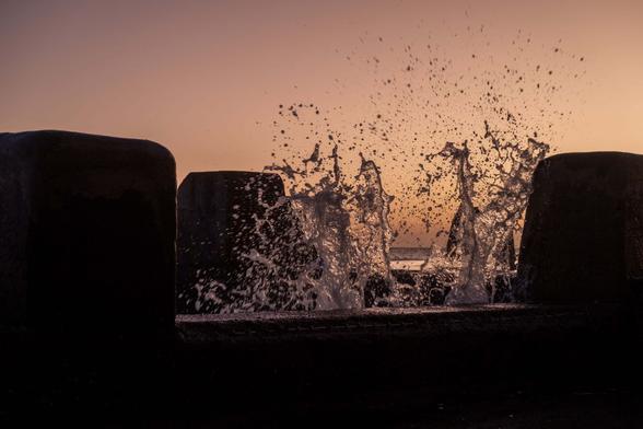 Splash on a wall of an ocean pool with the sunrise behind.