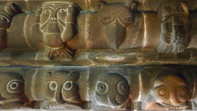 Simple carvings of the faces of owls, humans, owls, other animals, and more owls, haunting in the half-light.