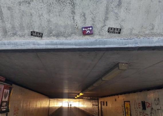 Small red/blue tile with bunbun, the rabbit on it. Bunbun is white, long wavy ears, running towards the right, and a slight smile on his face,

The tile is stuck to the outer edge of a tunnel (the "Daalsetunnel"), that can be seen in the lower two-third of the picture, with a grey concrete roof, and walls with white tiles on both sides, and two cyclists riding at the end of the tunnel, riding into the light at then end of the tunnel.