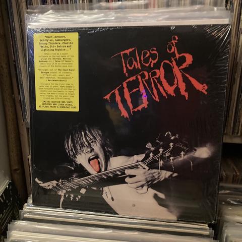 Tales of Terror in red text with the guitarist pictured engaging in “hot shot guitar” antics licking the back of his guitar neck while undoubtedly laying down face ripper of a solo