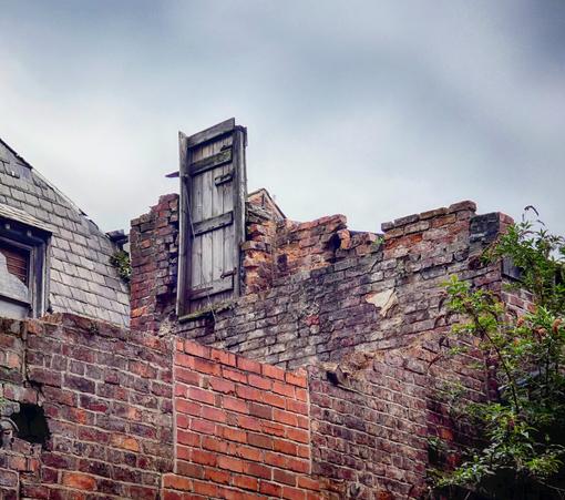 A photo of an intact, old wooden door in a heavily broken wall on one of the upper floors of a building.