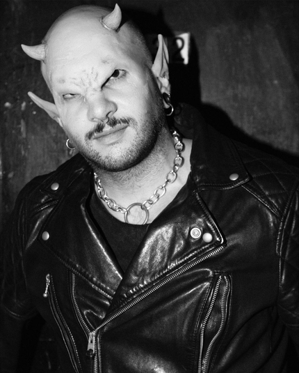 Picture of a man with demon prosthetics on his forehead and ears, he is dressed in leather and wear a chain
