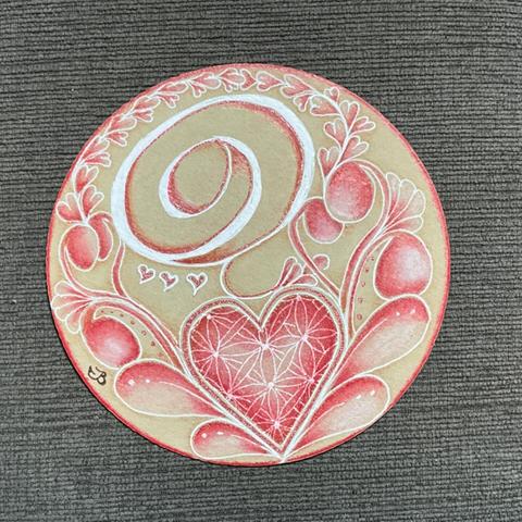 A Zentangle art tile. This is done on renaissance tan Zendala (circle tile), with a white gelly roll pen, 4 shades of red coloured pencils, and a red metallic pen. The image has a large heart shape in the bottom, with leafy like patterns  growing from it around the tile. In white and red is an abstract G shape in the upper half of the tile