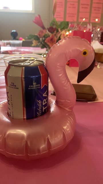 A can of beer in a mini flamingo pool floatie sitting on a pink table