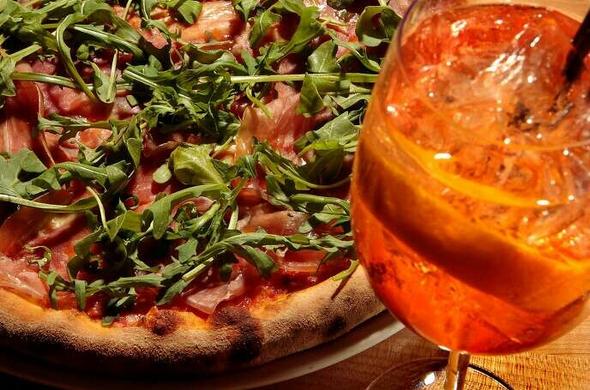 Prosciutto pizza next to a classic Aperol Spritz drink