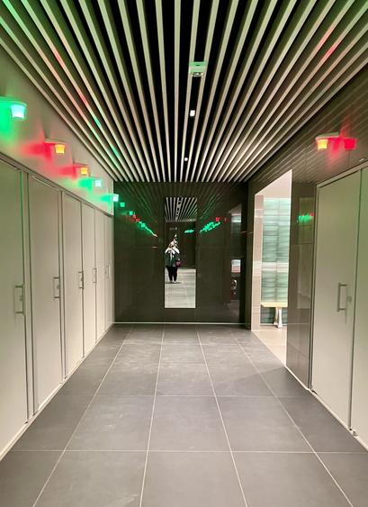 Completely closed bathroom stalls with green lights if available and red lights if occupied. End of walkway has a full length mirror.
