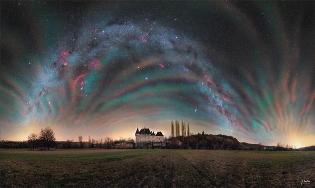 The sky over a picturesque chateau in France is shown featuring colorful airglow all around. Identifiable in the background night sky are objects that include the Orion Nebula, Sirius, Mars, and an arching band of our Milky Way Galaxy.