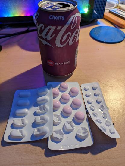 A can of cherry coca cola sits behind a trio of blister pack strips of pills, left is cocodamol, middle is ibuprofen & right is prochlorperazine.