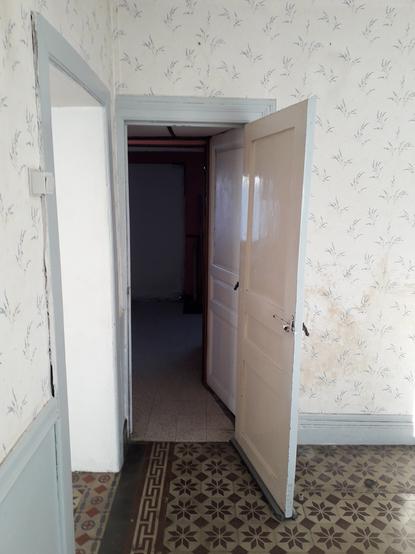 An open door in an old house linking two room one with colorful tiles on the floor, the other with plain white tiles stained by time.