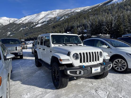 White jeep in the parking lot of a ski resort with blue skies and mountains in the background.