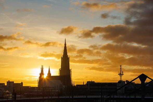 Das Ulmer Münster im Gegenlicht an einem goldenen Morgen mit Wolken.