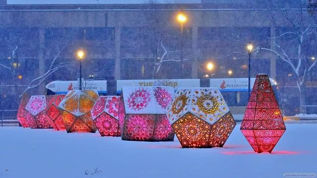A set of 8 light sculptures in a snowy park in Milwaukee, Wisconsin with The Hop streetcar behind it; snow is falling in a storm.