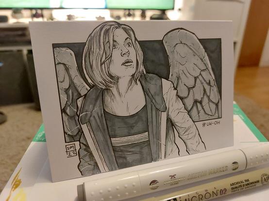 An ink drawing on folded card of the 13th Doctor being turned into a Weeping Angel. The Doctors face show shock and concern as the stone forms across her and the Angel wings form on her back.
