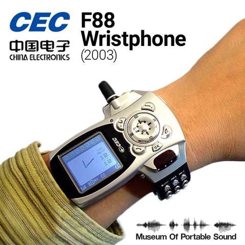 Closeup view of a wrist wearing the F88 wristphone. The phone looks very much like a 1990s Nokia brick phone torn apart and reassembled to fit on a wrist, with its touchtone buttons on a blue wristband, a circular input control where a watch face would normally be, and the screen of the phone jutting out to the left (or up the side of the arm) of where a watch face would normally be. At a 90 degree angle to the screen, a stubby cellular antenna juts out the side of the watch. It is simultaneously hilarious, ugly, and beautiful.