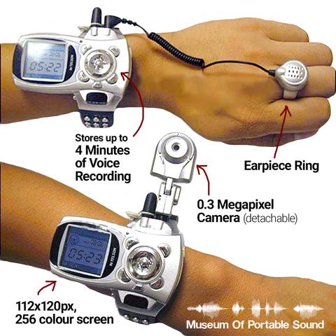 Two more views of a wrist wearing the wristphone. The first shows a minijack cable plugged into the phone next to its antenna, connecting to a large silver ring with a speaker grille inside a circular housing. A caption reads "Earpiece Ring". Another caption points at the body of the phone and reads "Stores up to 4 Minutes of Voice Recording".

The second wrist view shows the camera accessory plugged into the side of the phone just next to its antenna. It is nearly as large as the watch itself, with a joint below the lens to allow the camera to be positioned along a 180 degree axis. A caption reads "0.3 Megapixel Camera (detachable)". Another caption points at the phone screen, reading "112x120px, 256 colour screen".