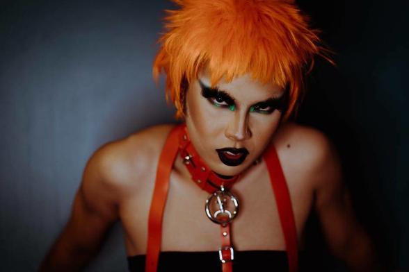 Una modelo fetish, con un collar y una traílla al cuello, maquillaje oscuro y peluca naranja