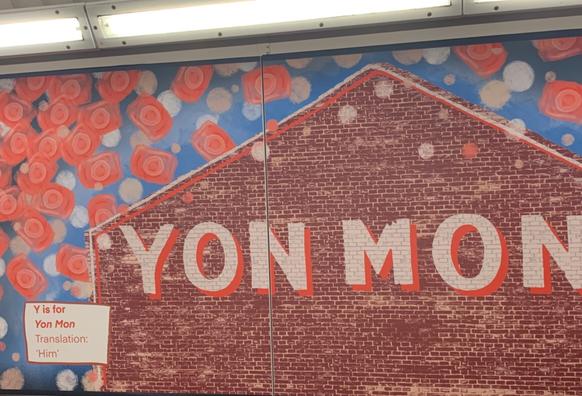 A brick house surrounded by a blue red and white background with the words ‘yon man.’ Y is for Yob man. Translation ‘him’