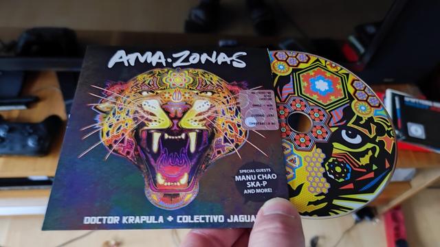 Amazonas steht groß am oberen Rand der CD Hülle, darunter ein Jaguar Kopf in bunten Farben, das Maul ist geöffnet, die Reißzähne zu sehen.
Unten steht Doctor Krapula + Collectivo Jaguar, dort wird die Hülle von einem Daumen gehalten.
Rechts schaut die CD über die Hälfte aus der Hülle hinaus, auch diese zeigt einen bunten Jaguar Kopf, dieser mit stilisierten Mustern darauf.
Der Hintergrund ist verschwommen.