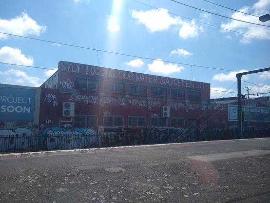Large paint lettering on a big brick building as seen from Burnley station saying "STOP LOGGING OUR WATER CATCHMENTS"