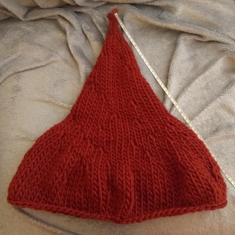Red knitted hat on a grey background with a tape measure showing that the hat is approx. 80cm long
