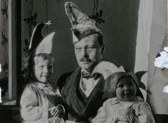 Schwarz-weiß Fotografie, der Großherzog mit seinen beiden Söhnen auf dem Schoß, alle drei tragen Narrenkappen
