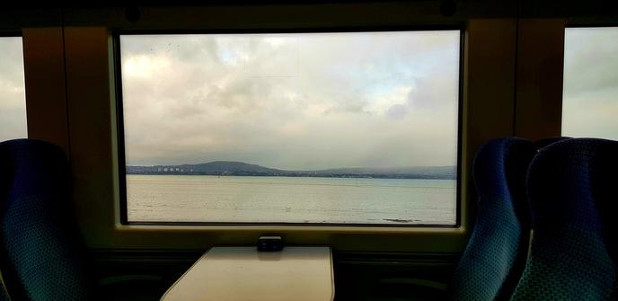 Photo through a train window near Holywood Northern Ireland showing Belfast Lough with hills and cloud in the background. Train seats and table in foreground.