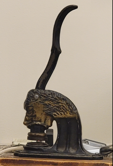 An antique cast iron lion's head press handle stamp seal press. The mouth holds the seal.