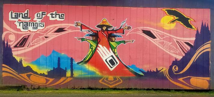 Land of the Namgis First Nation art mural with woman in red dress with two male figures flanking on both her sides.