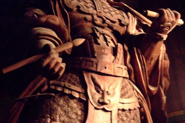 In brown tone due to poor lightning, a slightly blurry shot of the wooden statue midriff, with only the abdomen, belt, arms, brush and scroll in hands