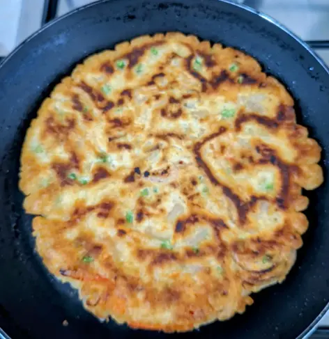A whole, browned Jeon (Korean pancake) in a small, black frying pan.