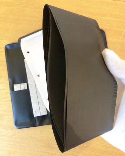 The white gloved hand holding up the dictabelts, now removed from inside the wallet. They are loops of material, and look like they might be big enough to fit on someone's head like a crown (or 1980s exercise headband)