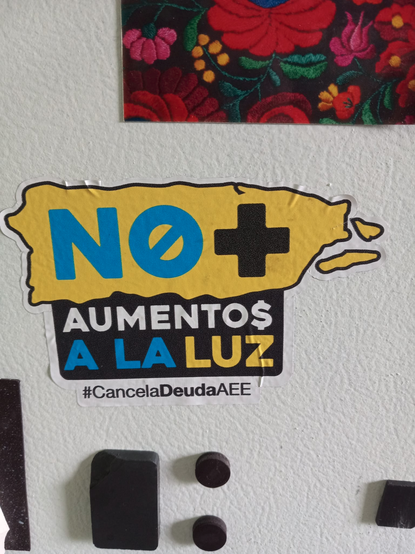 Sticker on refrigerator, a map of Puerto Rico reading:
N0+ AUMENTO$ A LA LUZ
#CancelaDeudaAEE
No price increases for electricity
#CancelPREPADebt