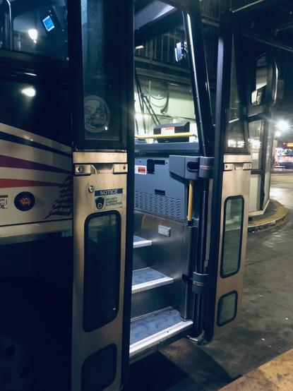 doors are ajar, entry stairs lit, on a driverless bus parked inside Port Authority, Manhattan.