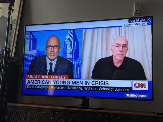 Scott Galloway being interviewed on TV. The lower-third, the text describing the segment, states "American young men in crisis," with the subtitle of "single and lonely."