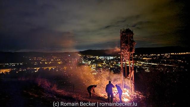 A bonfire burns, some persons are seen in front of it.