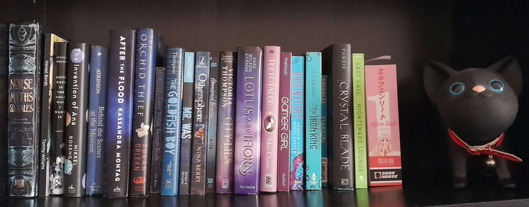 Another one of my bookshelves, containing the books: Norse Myths & Tales, Honest Bonds, Both Ways is the Only Way I Want It, The Invention of Ana, Behind the Scenes at the Museum, After the Flood, The Orchid Thief, Space Station Seventh Grade, The Goldfish Boy, Mr. Was, Othersphere, Abandoned Breath, City of Lies, Lotus and Thorn, Teetotaled, Gamer Girl, Originators (I only have book 2), The Iron King, Star Girl, The Crystal Blade, Last Call at the Nightshade Lounge, and the volume 1 omnibus of Elfen Lied! There's also a black cat piggy bank on the shelf. It's never been used as a piggy bank though since the head (the way you take the money out of it) is a bit defective. So it's just a statue...