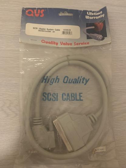 A DB25 to CN50 SCSI cable still in it’s original packaging! The plastic bag itself reads “High Quality SCSI CABLE”. The cardboard bit at the top which staples the plastic together reads “QVS Quality Value Service”. At the top right is a picture of a Mac printer/modem cable coming out of an apple (the fruit) and the words “LIFETIME WARRANTY”