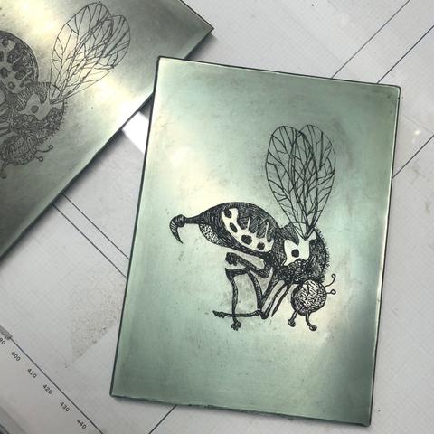 Photo of two etched shiny photopolymer plates of a wasp with carbon black printing ink remaining in the lines.